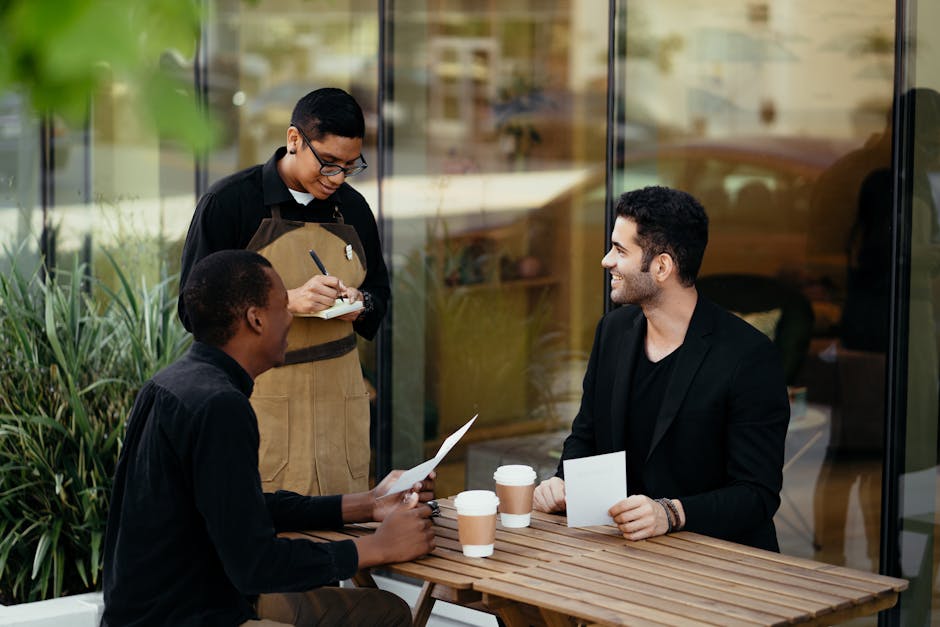 Two men meeting at an outdoor café, served by a waiter, exchanging ideas over coffee.