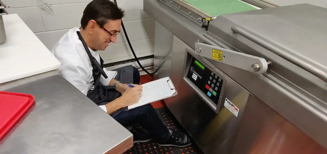 Chef Eric programming a double-chamber vacuum packaging machine in a commissary production kitchen