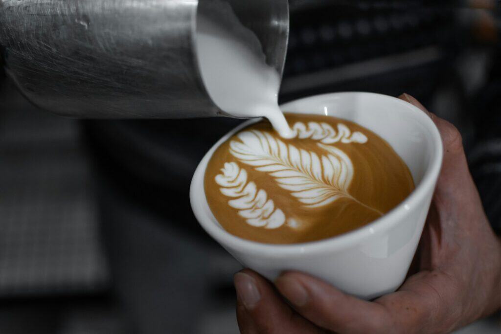 Barista pouring latte art into cappuccino in a coffee shop setting