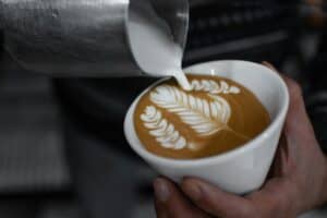 Barista pouring latte art into cappuccino in a coffee shop setting